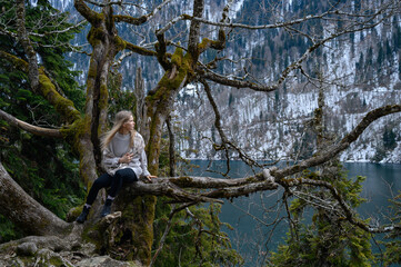 Girl sits on a tree and meditates on blue lake background. Lake Ritsa in Abkhazia