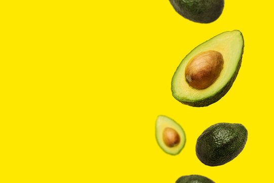pitted avocado and whole avocado fly in the air on a yellow background. Top view, flat lay