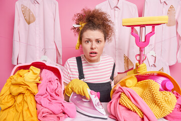 Routine work and household concept. Worried impressed housewife with curly hair holds mop poses...