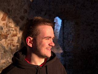 Young guy in a black tracksuit on the street, smiles and looks towards the sun, he's inside an old mill, sports life concept