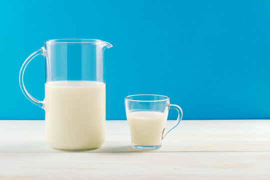 A jug and a glass of milk on a wooden table, on a blue background.