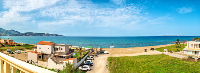 Panoramic photo of the seaside, with blue sea and sky, some houses and cars. 