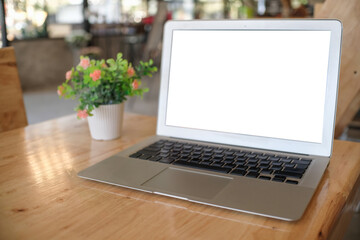Fototapeta premium Laptop with Mock up blank screen on wooden table in front of coffeeshop cafe space for text. product display montage- technology concept