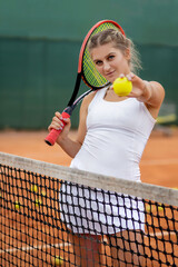 Athletic woman standing near net on court with racket in hands