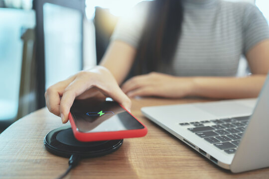 Woman Charging Mobile Phone With Wireless Fast Charger Pad On Desktop..