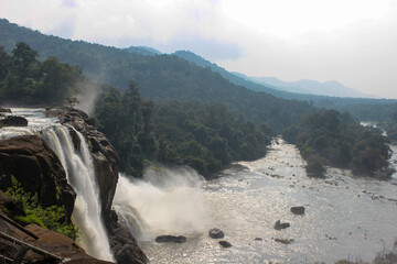 A Panoramic view of the dramatic waterfall flowing  majestically down and joining the river against the picturesque landscaped hills in the background near Kochi in India.
