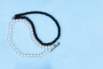 White and black pearl beads are laid out in the yin-yang sign on a blue textile background. Contrasting background with pearl jewelry.