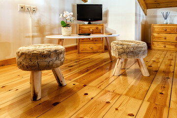 Part of living room. Two small three leged backless stools with on the wooden floor, at the ...