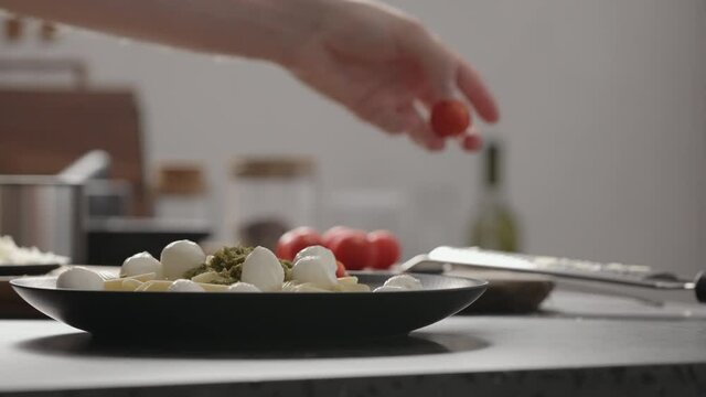 Slow motion orbit shot of man add cherry tomatoes to pesto penne on black plate
