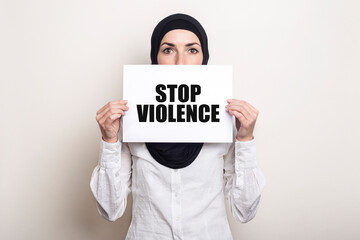 Muslim young woman in hijab covers her face with a banner with the text STOP VIOLENCE