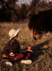 Little girl plays with horse in forest. Girl feeding apples to ponies outdoors.
