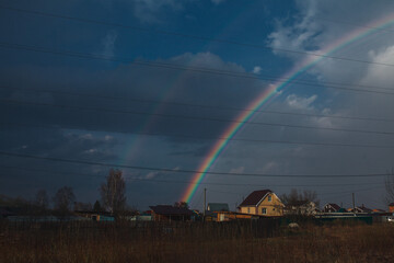 Rainbow over the village. Rainbow and cloudy sky.