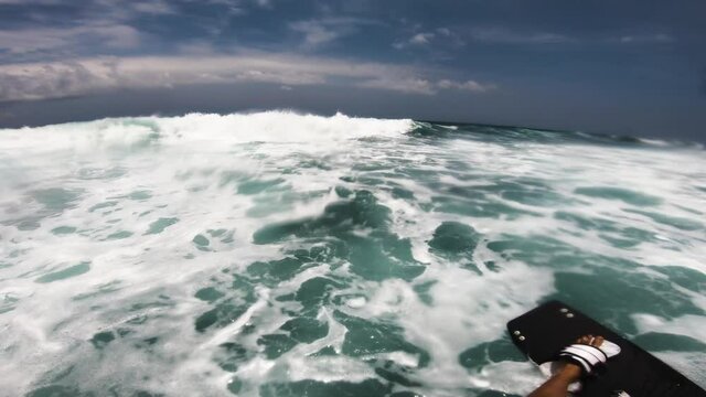 Pov shot of kite surfer jumping over high waves during dramatic cloudscape in background.