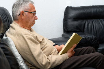 Fototapeta premium Man with glasses reading a book on the sofa