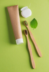 Two bamboo toothbrushes, toothpaste, dental floss and a leaf on green