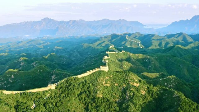 Aerial shot of Great Wall of China and surrounding green mountains under sun
