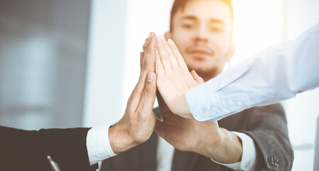 Business people group showing teamwork, joining hands and giving five to each other in sunny office