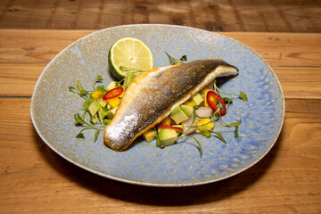 A delicious plate of fish Sea Bass with Mango and Avocado Salsa on a wooden kitchen table