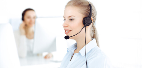 Blond woman call operator is using computer and headset for consulting clients online. Group of diverse people working as customer service occupation. Business concept