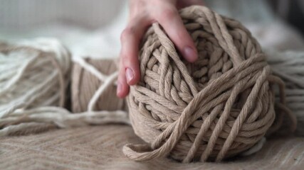 Boho-style wool threads lie on the bed, a woman's hand takes a ball. Suitable for macrame, banners and craft advertisements.