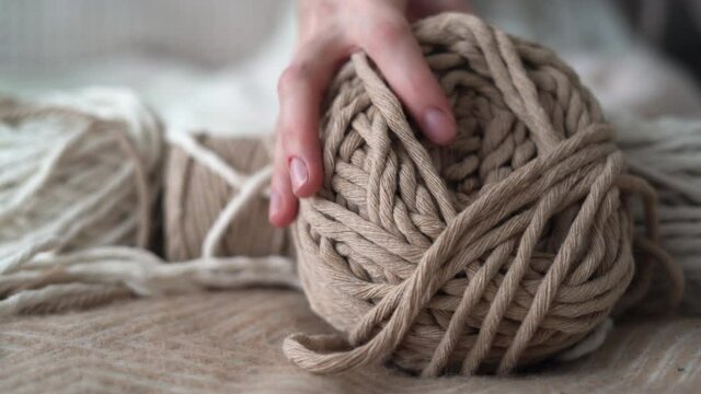 Boho-style wool threads lie on the bed, a woman's hand takes a ball. Suitable for macrame, banners and craft advertisements.