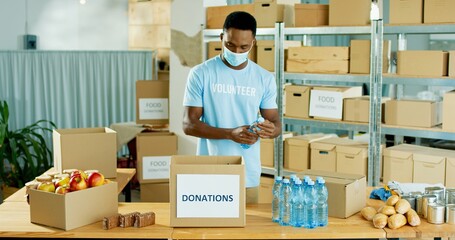 African American young handsome happy male warehouse worker volunteer working in shipping delivery charitable stock organization packing donations box Donating and volunteering, charity center concept