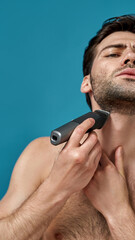 Portrait of brunette naked man looking focused while using electric razor isolated over blue background