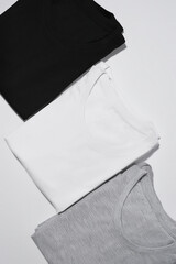 Three folded monochrome t shirts gray, black and white isolated over gray background