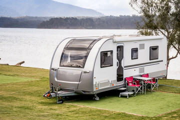 RV caravan camping at the caravan park on the lake with mountains on the horizon. Camping vacation travel concept - obrazy, fototapety, plakaty