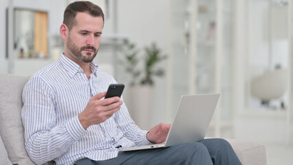 Hardworking Young Man using Smartphone and Laptop at Home 