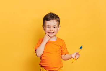 Happy baby toddler boy brushing his teeth with a toothbrush on a yellow background. Health care, oral hygiene.