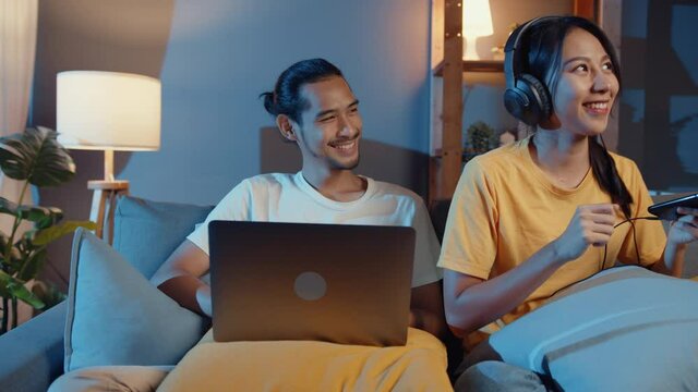 Freelance asia couple man and woman in casual hasband work  laptop computer at night enjoy happy relax with wife wear headphone listen music in smartphone sing dance on couch at house, Married life.