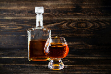 Glass flacon and wineglass with cognac on wooden plank surface.