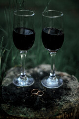 Red wine in glass glasses on a round, brown tree stump in the woods. Green grass on the background.
