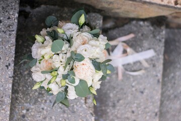 Beautiful bridal bouquet of white flowers and greenery, decorated with long silk ribbon lies on a gray textural background. Copy space