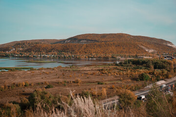 Beautiful autumn landscape. River valley. On the right is a large mound. Hill. A winding river. The colors of autumn. Brown, Red, Orange, Yellow, Turquoise. Blue lakes. A winding highway.