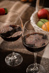 Red wine in large glass glasses foams on a brown tattered blanket. Next to it are ripe red, orange and green fruits in a basket.
