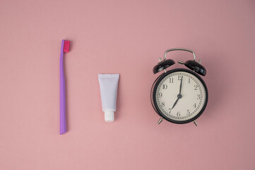 Fototapeta na wymiar Toothbrush, tube of toothpaste and alarm clock on a pink background. Time to brush your teeth.