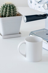 Mockup white ceramic mug with coffee machine and cactus on white table in vertical view.