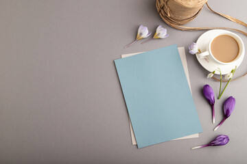 Blue paper sheet card mockup with spring snowdrop crocus and galanthus flowers and cup of coffee on gray background. top view, copy space.