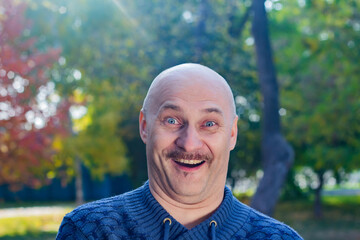 Portrait of a bald man with positive emotions in a blue sweater