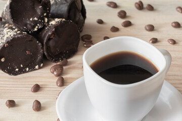 White cup of coffee with chocolate tubes and chocolate peanuts on wooden table top close up