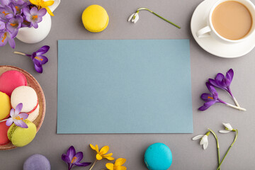Blue paper sheet mockup with spring snowdrop crocus flowers and multicolored macaroons on gray pastel background. top view, copy space.