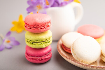 Fototapeta na wymiar Multicolored macaroons with spring snowdrop crocus flowers and cup of coffee on gray pastel background. side view, close up, selective focus.