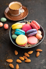 Different colors macaroons and chocolate eggs in ceramic bowl, cup of coffee on black concrete background. side view, close up.