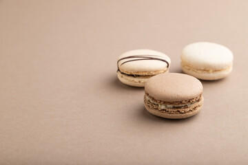 Brown and white macaroons on beige pastel background. side view, copy space.