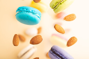 Different colors flying macaroons and almonds frozen in the air on blurred beige background. top...