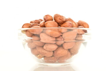 Organic peeled peanuts in a glass bowl, close-up, isolated on white.
