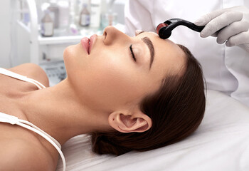 Beautician doing skin treatment using a microneedle dermaroller. Woman having procedure skincare with micro derma facial roller - obrazy, fototapety, plakaty