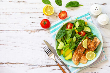 Grilled salmon fillet close-up with spinach, cucumber, tomato and avocado salad on a white wooden table. Top view, flat lay. Copy space.
